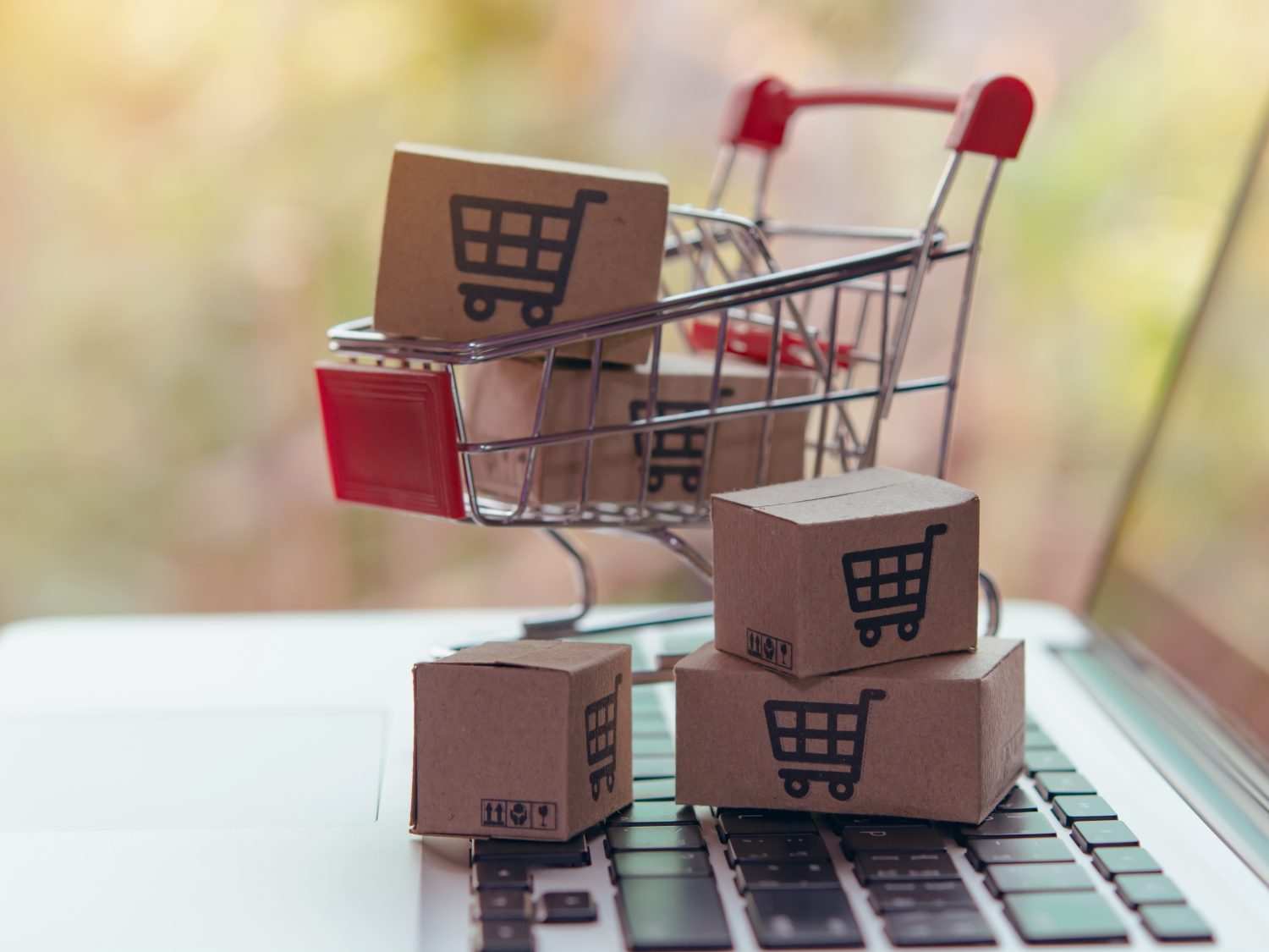 Shopping cart with boxes in it atop a laptop computer.