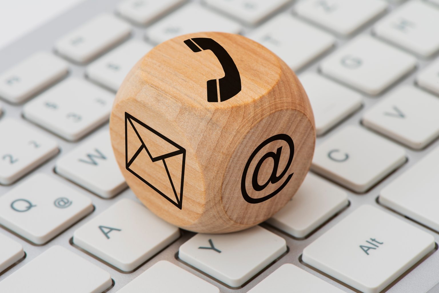 A wooden block with icons for phone, email, or web site on a laptop keyboard.